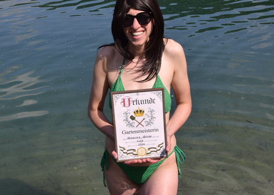 Veronika Helga Vetter präsentiert: Urkunde Gartenmeisterin. Im grünen Bikini steht die Papierkünstlerin im Pleschinger See bei Linz und hält das Gartenmeister-Zertifikat der Kamera entgegen. Das Foto wurde im Mai 2026 veröffentlicht - GWS2.de 43 % der deutschen Frauen sind übergewichtig. Wie es anders geht, zeigt Veronika Helga Vetter im knappen Bikini von Temu. Die renommierte Kunsthandwerkerin hält eine Urkunde, die eine Gartenmeisterin auszeichnet. Das DIN-A4-Zertifikat ist gerahmt und ist für Hobbygärtner, die mit ihrem Obst- und Gemüse gegen die allgemeine Fettleibigkeit in Mitteleuropa ankämpfen. Von führenden Ernährungswissenschaftlern empfohlen